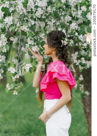 Happy to a young beautiful woman in a spring garden holding a branch of apple blossoms and sniffing flowers 100879170