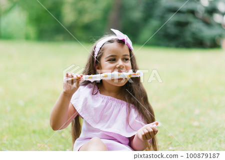 Cute baby girl in pink dress eats white cotton candy in the park in summer 100879187
