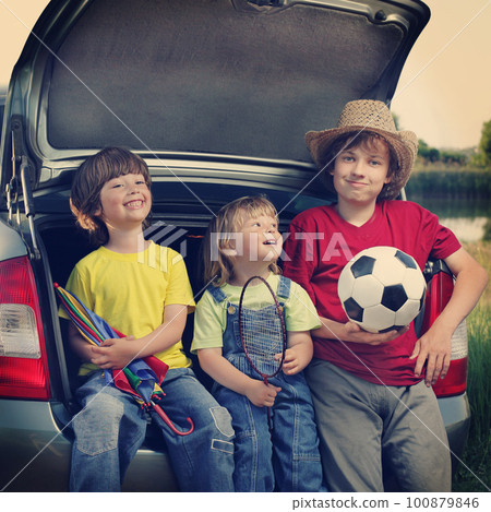 Three cheerful child sitting in the trunk of a car on nature 100879846