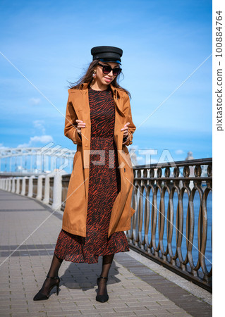 Beautiful woman in a cap and jacket posing while standing on the embankment 100884764