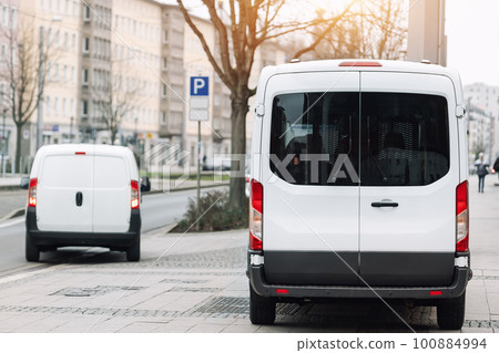 Small cargo delivery van parked in european city central district. Medium lorry minivan courier vehicle deliver package at residential office building in downtown area. Commercial shipping logistics Small cargo delivery van parked in european city central district. Medium lorry minivan courier vehicle deliver package at residential office building in downtown area. Commercial shipping logistics 100884994