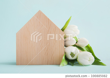 Model of wooden house and bouquet of white tulips on blue background close-up and copy space 100885082