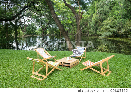 Sunbed chairs and table on green grass garden by pond 100885162