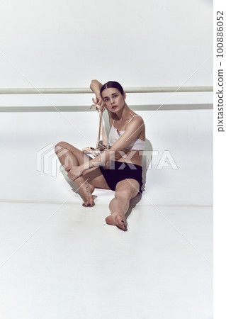 Adorable ballerina leaning on dance bar and resting after hard work in dance hall over white background 100886052