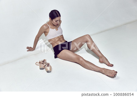Tired ballerina sitting on floor and resting after hard work in dance hall over white background Tired ballerina sitting on floor and resting after hard work in dance hall over white background 100886054