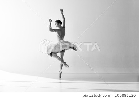 Monochrome. Ballerina wearing tutu poses in motion showing ballet elements while standing on pointe shoes over white backgrounds Monochrome. Ballerina wearing tutu poses in motion showing ballet elements while standing on pointe shoes over white backgrounds 100886120