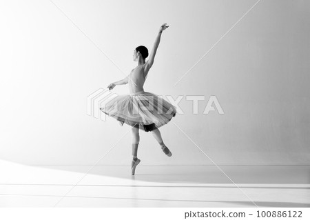 Monochrome. Ballerina wearing tutu in motion showing ballet elements while standing on pointe shoes over white backgrounds 100886122