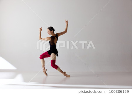 One young ballerina wearing pointe shoes dancing on fingertips over white background 100886139