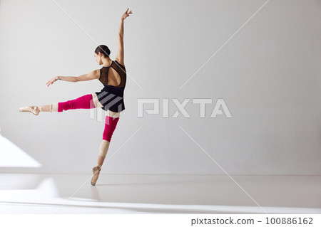 Back view. One beautiful ballerina wearing pointe shoes and demonstrating flexibility with graceful hand movements over white background Back view. One beautiful ballerina wearing pointe shoes and demonstrating flexibility with graceful hand movements over white background 100886162