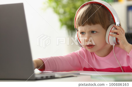 Little girl child in headphones in front of laptop Little girl child in headphones in front of laptop 100886163