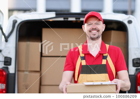 Smiling male courier pulling box in background of car Smiling male courier pulling box in background of car 100886209