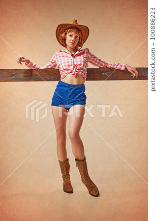 Attractive, pretty, young girl in checkered shirt and cowboy style hat posing against brown background. Country style 100886223