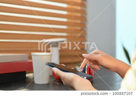 Side view of woman hands typing on smart phone while sitting in modern creative office Side view of woman hands typing on smart phone while sitting in modern creative office 100887107