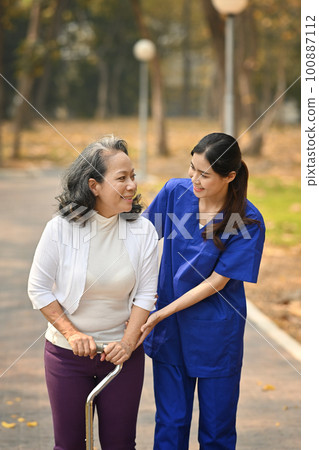 Careful caregiver taking care of elderly woman patient during walking outdoor. Assistance and rehabilitation concept Careful caregiver taking care of elderly woman patient during walking outdoor. Assistance and rehabilitation concept 100887112