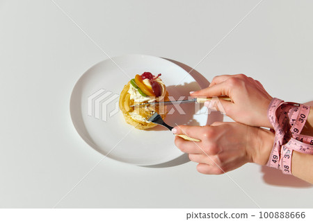 Top view of female hands tasting sweets with bound hands over white background. Junk food, cheat meal, eating disorder Top view of female hands tasting sweets with bound hands over white background. Junk food, cheat meal, eating disorder 100888666