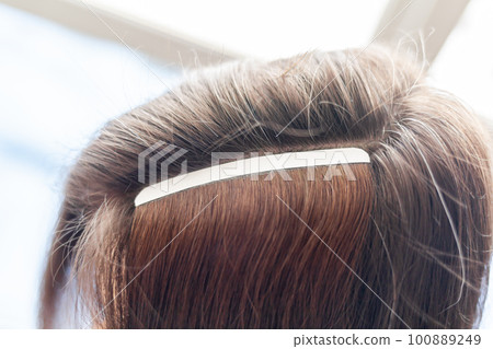 Hair ribbons for extensions on a woman's head at home. Hair extensions to thicken your own. Individual strands of hair close-up Hair ribbons for extensions on a woman's head at home. Hair extensions to thicken your own. Individual strands of hair close-up 100889249