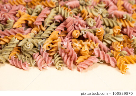 Rice vegetable pasta in the form of spirals on a white background. Healthy rice pasta with tomatoes, selenera, carrots and beets 100889870