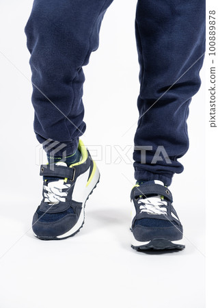 Childrens shoes. Blue kids running shoes sneakers on the legs of a five- or six-year-old boy on a white background. Childrens shoes. Blue kids running shoes sneakers on the legs of a five- or six-year-old boy on a white background. 100889878