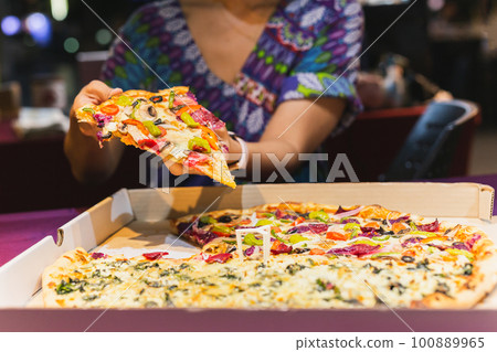 Woman hand taking a slice of New York pizza in takeaway box. Woman hand taking a slice of New York pizza in takeaway box. 100889965