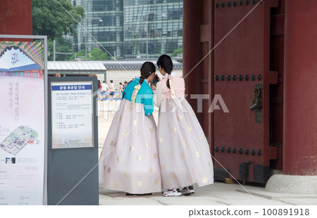 在韓國首爾的旅遊景點景福宮租來的幾位年輕女性穿著 chima jeogori 看著他們的智能手機 100891918