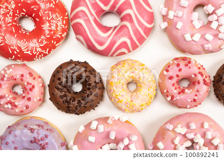 Many different donuts on a white background top view, pink, white and chocolate donuts of different sizes 100892241