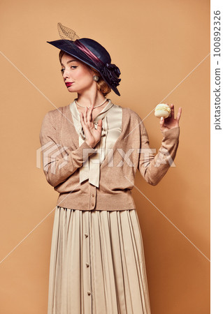 One beautiful woman wearing retro style clothes holding cake with unpleasant facial expression over beige background 100892326