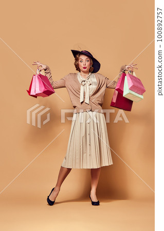 One charming woman wearing retro clothes holding paper bags over beige background. Sales, Black Friday concept One charming woman wearing retro clothes holding paper bags over beige background. Sales, Black Friday concept 100892757