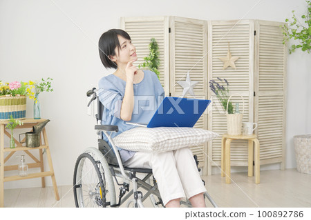 A woman in a wheelchair imagining while using a laptop in her living room 100892786