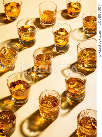 Whiskey and bourbon in luxury glasses with ice cubes on golden background. Whiskey and bourbon in luxury glasses with ice cubes on golden background. 100893007