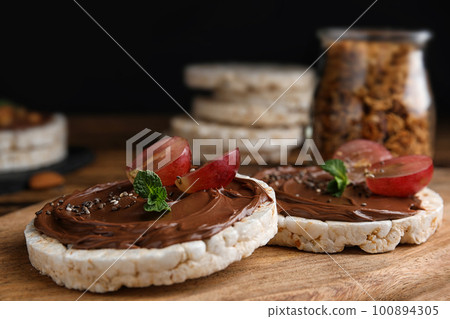 Puffed rice cakes with chocolate spread and grape on wooden board, closeup Puffed rice cakes with chocolate spread and grape on wooden board, closeup 100894305