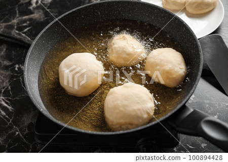 Cooking delicious donuts in hot oil, closeup 100894428