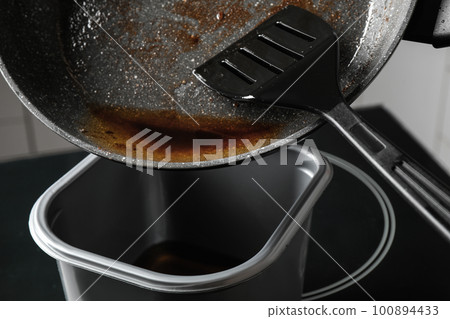 Pouring used cooking oil from frying pan into container, closeup 100894433