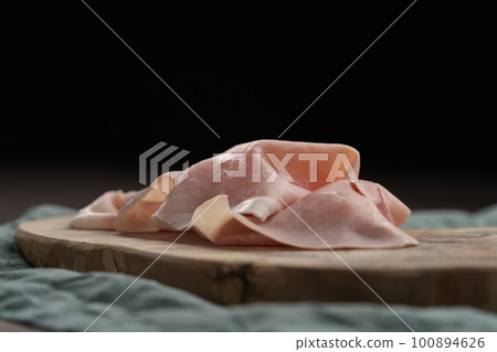 Thin slices of prosciutto cotto on olive wood board 100894626