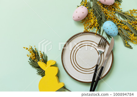 Easter table setting. Plate with easter eggs and mimosa on a pastel green background. Happy Easter holiday concept for restaurants. View from above. Copy space. Easter table setting. Plate with easter eggs and mimosa on a pastel green background. Happy Easter holiday concept for restaurants. View from above. Copy space. 100894784