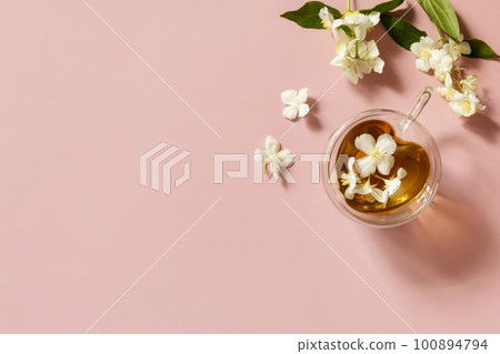 Cup of jasmine tea with jasmine flowers on a pink pastel background. Organic natural drinks concept. View from above. Cup of jasmine tea with jasmine flowers on a pink pastel background. Organic natural drinks concept. View from above. 100894794