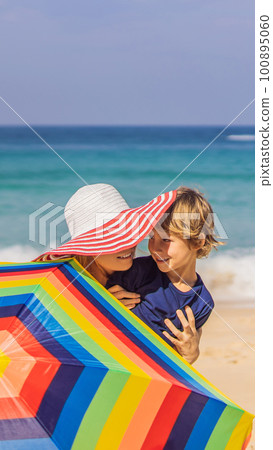 Mother and son on the beach in a hat and beach umbrella 100895060
