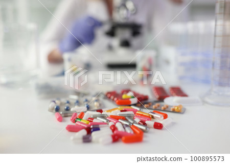 Pile of pills on white table against woman doing research Pile of pills on white table against woman doing research 100895573