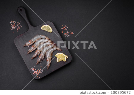 Tiger prawn or langoustine raw with spices and salt on a wooden cutting board Tiger prawn or langoustine raw with spices and salt on a wooden cutting board 100895672