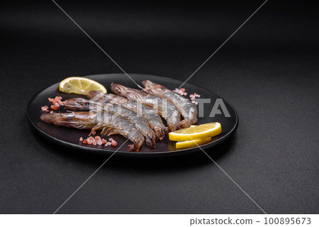 Tiger prawn or langoustine raw with spices and salt on a wooden cutting board Tiger prawn or langoustine raw with spices and salt on a wooden cutting board 100895673