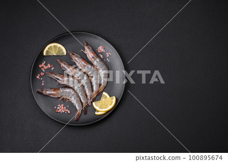 Tiger prawn or langoustine raw with spices and salt on a wooden cutting board Tiger prawn or langoustine raw with spices and salt on a wooden cutting board 100895674