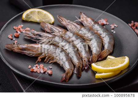 Tiger prawn or langoustine raw with spices and salt on a wooden cutting board Tiger prawn or langoustine raw with spices and salt on a wooden cutting board 100895678
