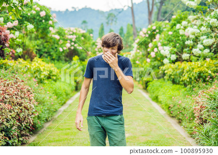 Young man blowing nose in front of blooming tree. Spring allergy concept Young man blowing nose in front of blooming tree. Spring allergy concept 100895930