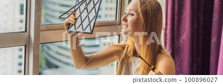 Young woman does makeup sitting by the window with a panoramic view of the skyscrapers and the big city BANNER, LONG FORMAT 100896027