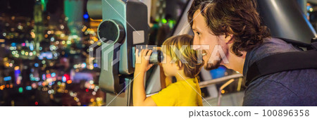 Dad and son are looking at Kuala lumpur cityscape. Use binoculars. Panoramic view of Kuala Lumpur city skyline evening at sunset skyscrapers building in Malaysia. Traveling with kids concept BANNER 100896358