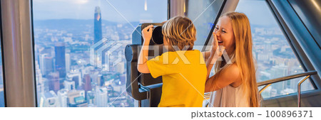 Mom and son are looking at Kuala lumpur cityscape. Use binoculars. Panoramic view of Kuala Lumpur city skyline evening at sunset skyscrapers building in Malaysia. Traveling with kids concept BANNER Mom and son are looking at Kuala lumpur cityscape. Use binoculars. Panoramic view of Kuala Lumpur city skyline evening at sunset skyscrapers building in Malaysia. Traveling with kids concept BANNER 100896371