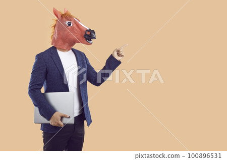 Businessman in horse mask holds laptop and points with his finger to place for advertising text. Businessman in horse mask holds laptop and points with his finger to place for advertising text. 100896531
