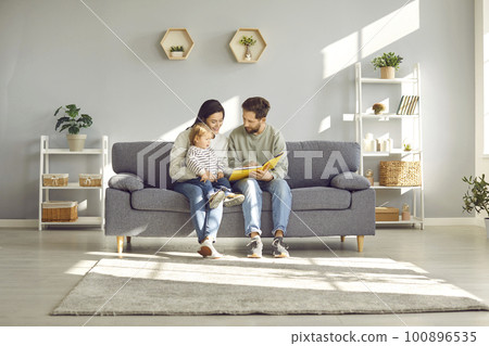 Loving young parents with their young child read a book together, sitting at home on cozy sofa. Loving young parents with their young child read a book together, sitting at home on cozy sofa. 100896535