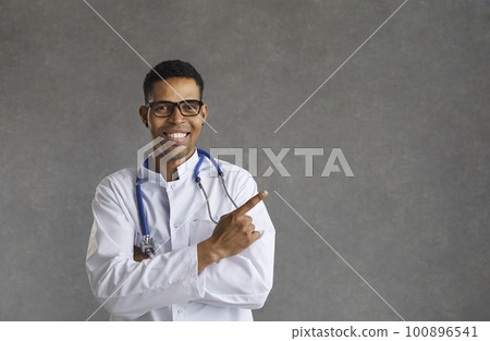 Friendly smiling male african american doctor pointing with finger aside 100896541