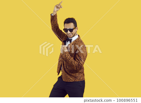 Funny young man in a leopard jacket and trendy sunglasses dancing isolated on a yellow background Funny young man in a leopard jacket and trendy sunglasses dancing isolated on a yellow background 100896551