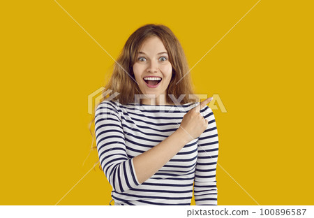 Young laughing excited woman with wavy hair is pointing on copy space on yellow background. Young laughing excited woman with wavy hair is pointing on copy space on yellow background. 100896587